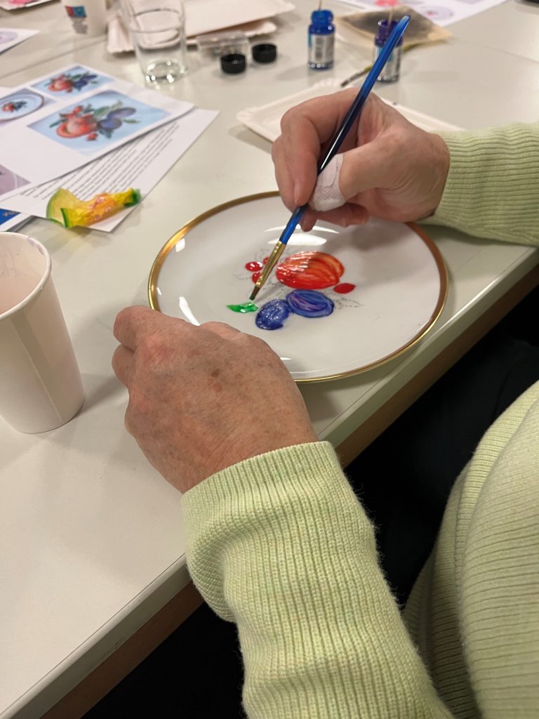Obst auf Porzellanteller Eine Hand malt bunte Motive auf einen weißen Teller.