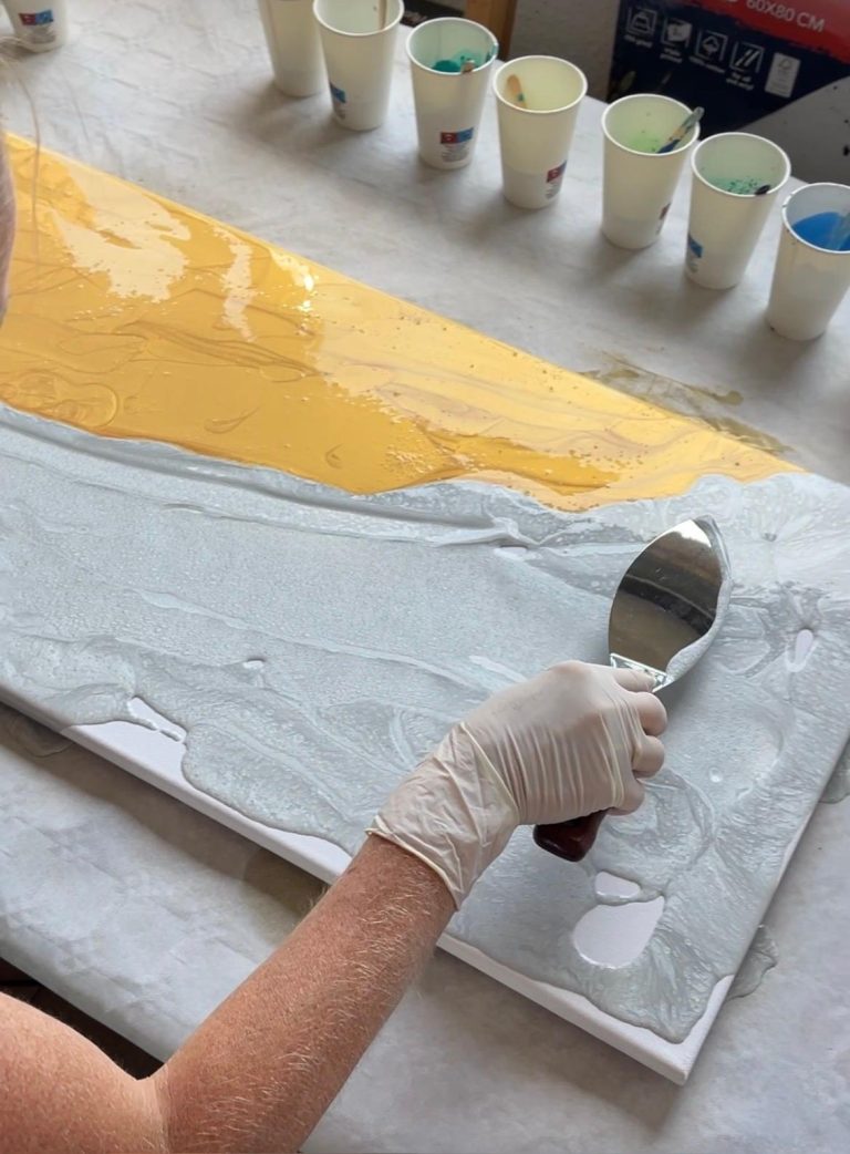 Eine Person trägt graue und gelbe Farbe auf eine Leinwand auf.