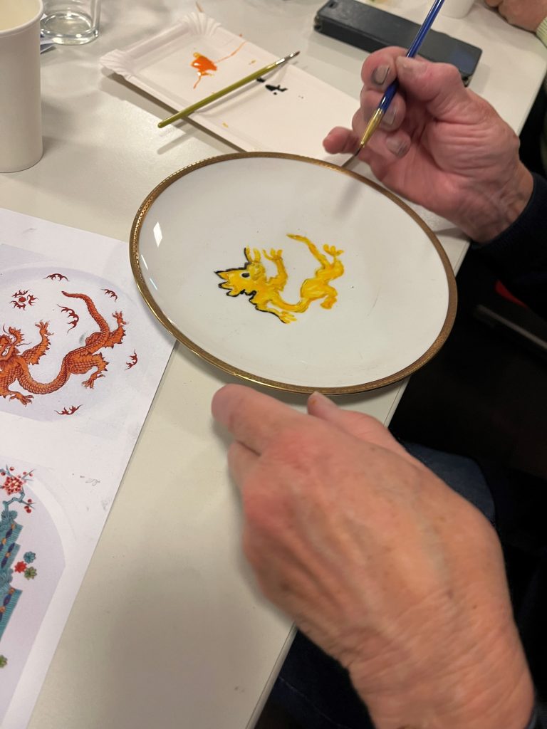 Drache auf Porzellan Eine Hand hält eine weiße Schüssel mit einer gelben Drachenzeichnung.