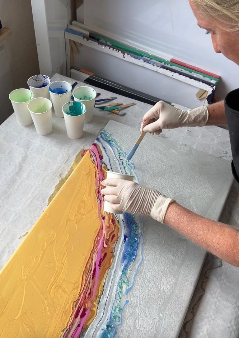 Eine Person trägt farbige Farbe auf eine Leinwand auf, um abstrakte Muster zu gestalten.